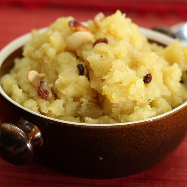 A brown bowl filled with Indian Sooji Halwa, garnished with cashews and raisins, on a red tablecloth.