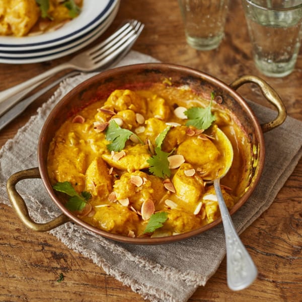 Indian chicken curry in a copper pan, garnished with cilantro and sliced almonds.