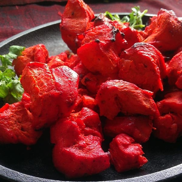 Bright red Indian chicken tikka pieces with green garnish on a dark plate.
