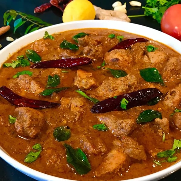 Indian chicken curry with dried red chilies and fresh herbs in a white bowl.